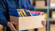 © twc - A person hold cardboard box filled with school supply, book, pencil, and stationery item for donation or relocation in storage room