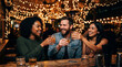 © Matos - Friends enjoying drinks and laughter at a bar with string lights