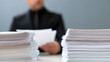 © photo for everything - Business professional sit at desk with large stack of paper document pile in modern office environment representing corporate task work load