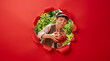 © ZaStock - Young boy peering through torn red paper holding large ripe tomato, garden background with sunflowers. Agriculture, organic farming, healthy eating, nutrition.