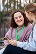 © Austockphoto - Teenage girl smiling happily while seated with a young adult woman on an urban bench