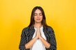 © Daniel - Young woman finding inner peace and practicing mindfulness, closing her eyes and holding hands in a prayer gesture against a vibrant yellow background