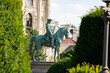 © VladyslavShcherbakov - Statue dominates. Horse carries rider. Architecture rises. Greenery frames monument.