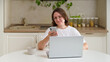 © Андрей Журавлев - Woman using smartphone and laptop at kitchen table. Woman is working from home in a bright, modern kitchen. This image is perfect for remote work or technology themes.