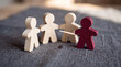 © The Stock Hub - Leadership concept with red wooden figure pointing at group of three natural wood figures on textured surface