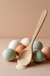 © Людмила Мазур - Wooden spoon filled with smooth batter, surrounded by fresh eggs in various pastel colors on a beige surface, suggesting baking preparation.