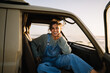 © Júlia Amaral - Woman smiles happily while sitting in a vintage van wearing denim overalls