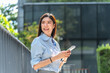 © Jestercine - Asian businesswoman leans against a metal railing outside her office and looks away from her smartphone during a short break on a sunny afternoon.