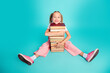 © deagreez - Smiling schoolgirl sitting on turquoise floor hugging a stack of books, happy child enjoying reading and learning