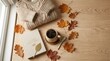 © safitri - A warm woolen sweater lies next to an open book and a steaming cup of coffee on a wooden table.