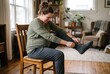 © Kassiopeia  - A pregnant woman sits on a wooden chair in her living room. She struggles to put on a sock while showing signs of discomfort. The room has natural light and plants