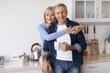 © Prostock-studio - Smiling Elderly Couple, Caucasian Man And Woman, Embracing Each Other In A Cozy Kitchen While Enjoying Morning Coffee. Togetherness And Happiness Captured At Home In A Simple, Loving Moment.