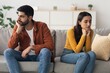 © Prostock-studio - Worried Couple, Young Adults, Mixed Ethnicity, Sitting On Couch With Distressed Expressions, Facing Away From Each Other In A Living Room, Experiencing Relationship Conflict, Emotional Concept.