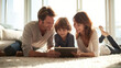 © syaifuddin - photorealistic lifestyle photograph of a modern family relaxing together in a bright home, parents and one child gathered naturally around a tablet while talking and smiling