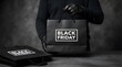© MSTHIRAMONY - Person wearing black gloves holding a black shopping bag with black friday text