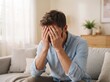 © Asad - Stressed man sitting on a sofa covering his face with his hands in a bright room mental health emotional pain living room depression overwhelmed frustrated suffering hopelessness