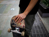 Hand of a male skateboarder wearing a black t-shirt with his skateboard on a cloudy day in Thailand
