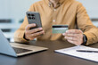 © Liubomir - Online payment and e commerce security, person using smartphone and credit card for digital banking transaction at office desk. Secure mobile app usage for financial management and shopping.