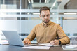 © Liubomir - Productivity and focus in the workplace, professional man working on laptop and writing notes at office desk. Business strategy and task management.