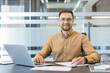 © Liubomir - Professional business success and corporate productivity, smiling man working on laptop and writing notes in modern office. Entrepreneurial mindset and career growth, office worker managing tasks.