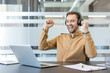 © Liubomir - Success and career achievement, happy man celebrating professional victory with laptop and headphones in modern office. Excited employee reaching goals and finishing projects with joy and motivation.