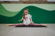 © qunica.com - A young girl sits in a middle split on a foam mat while focusing on her stretch. She practices flexibility and balance in a bright indoor gym setting.