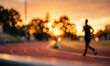 © BlurryBob - A silhouette of a runner on a track during sunset, with a beautiful bokeh effect highlighting the warm colors of the sky and tree outlines in the background.