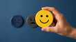 © MstMahmudaAktar - Person holding yellow smiling emoticon face sculpture against blue feedback wall
