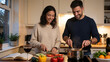 © Lubov - A happy young couple prepares a healthy meal together in a modern home kitchen. The woman slices fresh tomato while the man stirs a pot on the stove