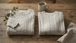 © Background - Two folded cream colored cable knit sweaters placed on a rustic wooden table with a steaming ceramic mug and a small green eucalyptus branch
