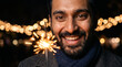 © Elvira - Happy man holding sparkler with bokeh lights at night celebration