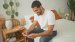 © Krakenimages.com - Man sitting on bed smiling and holding smartphone with bare forearms visible in a building, casual white tshirt and jeans; quiet contentment.