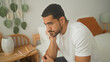 © Krakenimages.com - Young hispanic man with hand on chin sitting on bed beside notebook and lamp in a building; quiet contemplation.