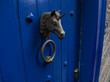 © TomKorcak - Close-up of a decorative brass unicorn head door knocker on a bright blue painted wooden door, traditional entry hardware detail.