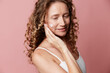 © SHOTPRIME STUDIO - Middle aged woman applies moisturizer to her cheek, natural skin visible, soft pink studio backdrop, candid beauty and selfcare concept for photography.
