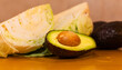 © Guillermo - Medio aguacate con carozo en primer plano, con trozos borrosos de col verde fresca en el fondo desenfocado.