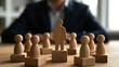 © pattozher - Leadership Metaphor: A wooden figure of a person stands tall on a raised platform, symbolizing leadership, surrounded by smaller figures representing a team.
