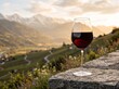 © Artsaba Family - Glass of red wine sitting on a stone ledge overlooking an alpine vineyard valley at sunset