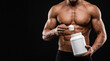 © mamo studios - Muscular shirtless bodybuilder preparing protein powder shake holding blank white supplement tub and scoop on dark background for sports nutrition fitness muscle growth and healthy lifestyle concept