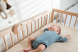 © leungchopan - Baby resting peacefully in a wooden crib on a striped sheet