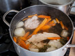 © Marek - Homemade chicken broth cooking in a large pot with chicken meat, carrots, onion and root vegetables, showing traditional soup preparation on a kitchen stove.
