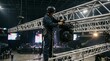 © Tech - A professional stage technician working on lighting equipment suspended high above a concert venue arena.
