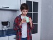 © Anastasiya - Teenage Boy Holding Mug in Kitchen. Thoughtful teenage boy in plaid shirt holding a green mug in the kitchen. Quiet contemplative indoor moment.