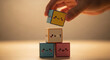 © GraphicX - A hand is seen holding a colorful stack of cubes with emoticons and mathematical symbols, indicating a playful and educational theme.