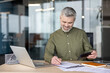 © Liubomir - Financial analysis and business planning, mature businessman using a calculator and writing on documents at his office desk with a laptop computer. Professional manager reviewing data and budget.