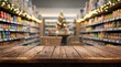 © Tina - Wooden table in focus with a blurred grocery store interior decorated with golden holiday lights and a Christmas tree during festive shopping season.