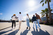 © CarlosBarquero - Bright outdoor scene of multicultural friends strolling away together across a modern promenade with palm trees, blue sky