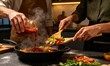© Renaldi saleh - Two adults prepare a flavorful meal together with fresh vegetables, chili sauce, and rising steam in a modern kitchen