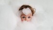 © Bonsales - Child playing in bath foam, big blue eyes peering curiously through many bubbles during hygiene time