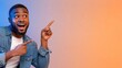 © xuxu - Excited african american man pointing fingers at copy space, looking at amazing offer or big sale on orange background